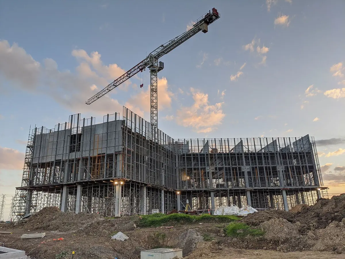 A multi-storey commercial building under construction beneath a tower crane at sunset
